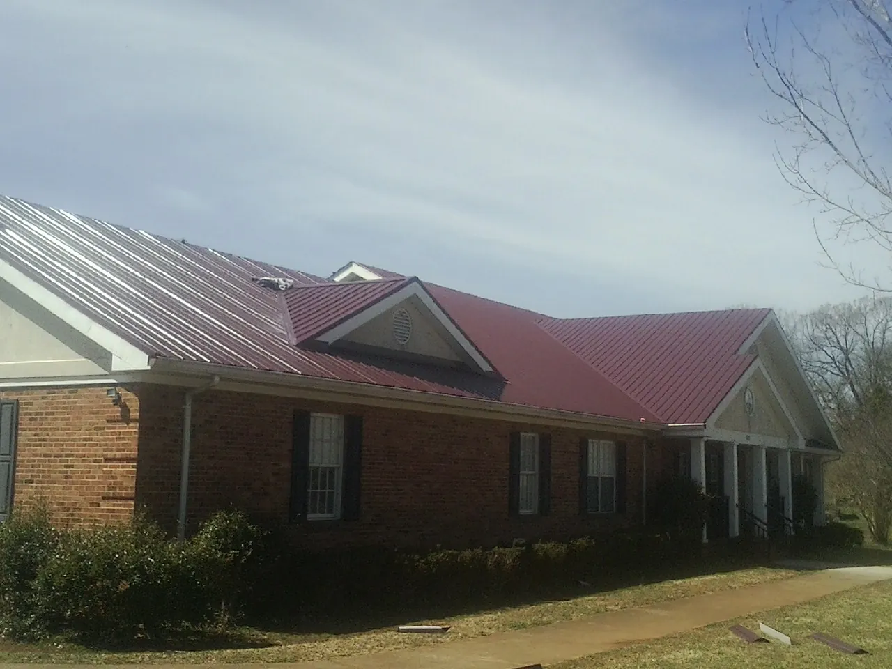 Red metal roof with gabled entries on a long brick building, from a Hail Damage Roof Repair job in El Dorado