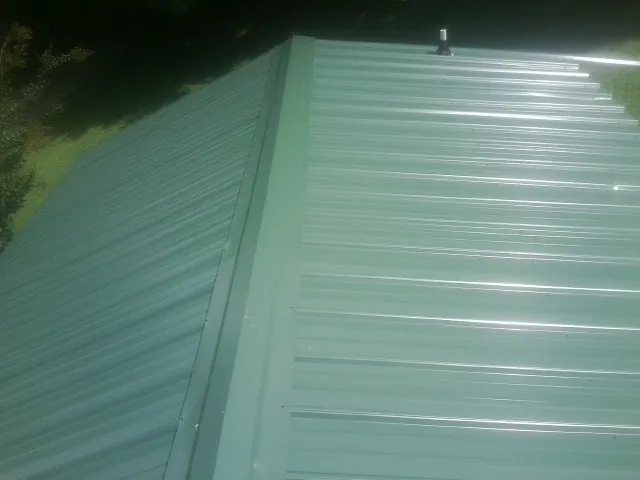 New green metal panels meeting at the ridge of a roof — Flat Roof Repair work by our crew in El Dorado