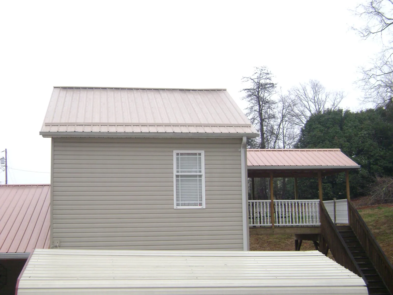 Tan metal roofs on a two story addition and attached porch, from a Roof Replacement job in El Dorado